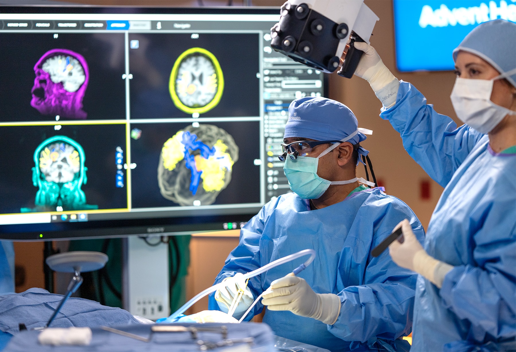Neurosurgeons in an operating room with a brain scan on a monitor behind them